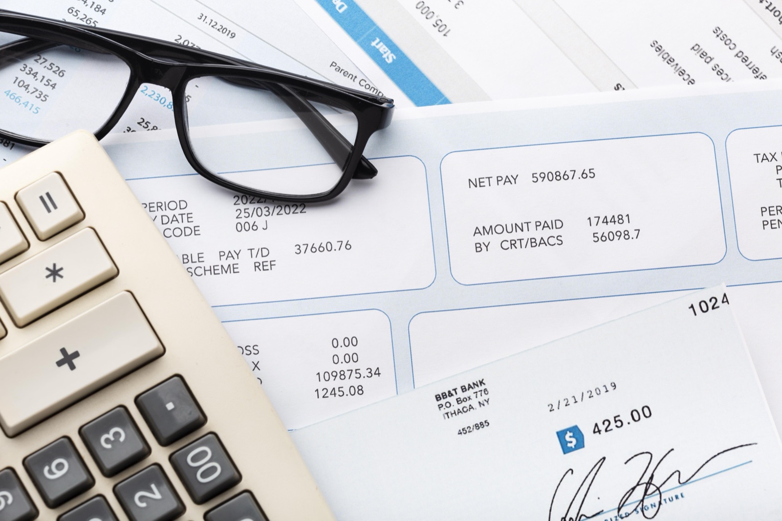 Fiche de paie, calculatrice et lunettes posées sur un bureau